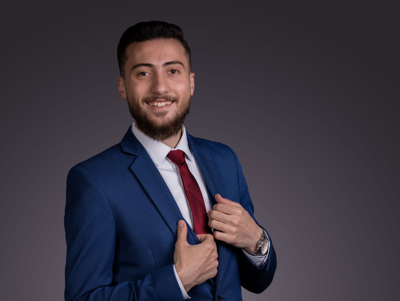 Confident young businessman in a blue suit and red tie, smiling with elegance.