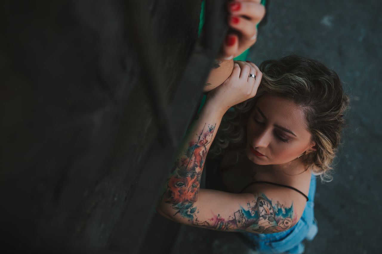 Aerial view of a woman with tattoos and spaghetti straps, captured in moody lighting.