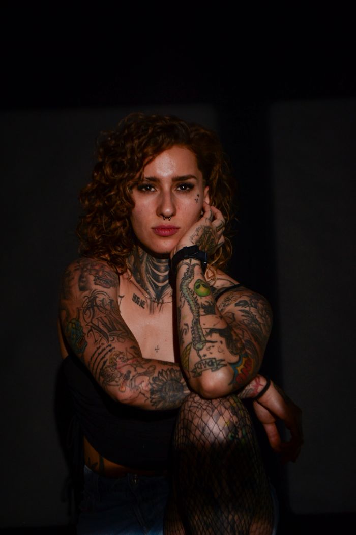 Portrait of a young tattooed woman with curly hair in a dramatic low-light studio setting.